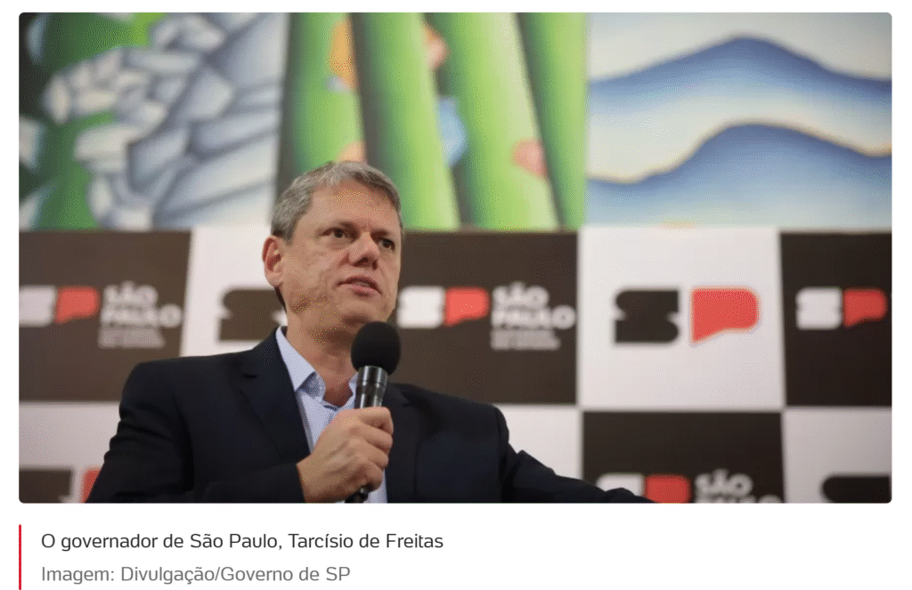 O governador de São Paulo, Tarcísio de Freitas, um homem branco de meia-idade, vestindo terno escuro, fala em um microfone que segura com a mão direita, com um painel gráfico do governo de SP ao fundo.